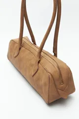 Cartera baguette color marrón claro, confeccionada en símil cuero con formato cilíndrico y doble asa corta.