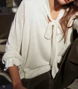 Blusa blanca de lino con lazo en el cuello y mangas largas con volados.