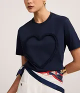 Remera azul marino de algodón con cuello redondo y mangas cortas. Presenta un aplique en forma de corazón con volados en el frente.