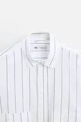 Camisa cropped fit confeccionada en tejido de algodón a rayas verticales negras sobre fondo blanco. Cuello solapa y manga larga acabada en puño con botones. Bolsillos frontales de plastrón con solapa. Cierre frontal de botonadura.