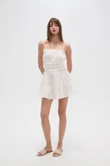 Vestido corto blanco de algodón con breteles finos, escote recto, corte holgado, volados en el ruedo y elástico en la cintura.