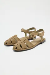 Sandalias cangrejeras planas de serraje color beige, con puntera redondeada y cierre de hebilla lateral ajustable.