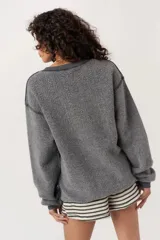 Sweater gris oscuro, de textura afelpada o tipo borreguito, con cuello redondo y puños y ruedo acanalados. Estampado frontal con texto en mayúsculas "WILD NIGHTS" y un dibujo de una copa de cóctel.