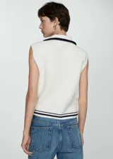 Chaleco de punto color crudo, con cuello polo y cierre de cremallera metálica. Tiene diseño sin mangas y ribete a rayas en el bajo.