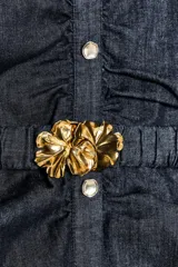 Vestido midi de denim azul oscuro, con cuello redondo y sin mangas. Presenta detalle de frunces en la cintura, cinturón elástico con hebilla dorada y cierre lateral con cremallera oculta. Tiene falsos botones delanteros.