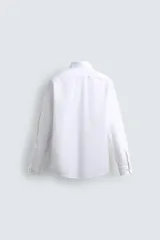 Camisa blanca de corte recto, con cuello italiano abierto, mangas largas con puños abotonados y cierre frontal con botones.