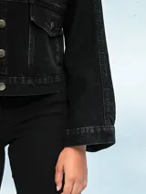 Campera de jean negra con corte cropped, cuello clásico, cierre frontal con botones metálicos y bolsillos con solapa en el pecho.