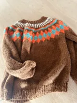 Sweater marrón tejido a mano en mohair con cuello redondo y diseño con motivos geométricos en colores blanco, rosa y celeste.