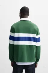Polo de rugby verde con rayas horizontales azules y blancas, cuello blanco con solapa y cierre de botones, y mangas largas con puños acanalados.