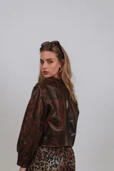 Campera bomber color beige de cuero, con cuello redondo, cierre frontal con botones a presión, mangas largas con puños elásticos y detalles de tachas metálicas en hombros y espalda.