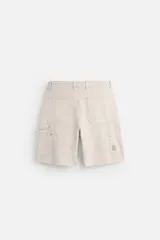 Bermuda color verde militar, de corte relaxed fit, con bolsillos frontales y traseros tipo plaqué, detalle de tira y bolsillo multifunción en la pierna, y bajo irregular.