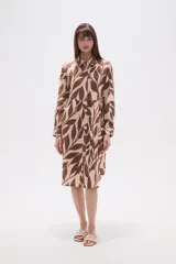 Vestido camisero midi holgado con estampado de hojas en tonos marrones y beige, cuello camisero y cierre frontal con botones.