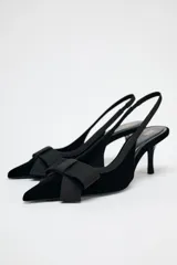Zapato destalonado de terciopelo negro con tacón fino y adorno de lazo en la parte delantera.