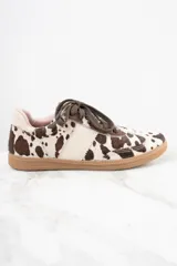 Zapatillas bajas con estampado de vaca en tonos marrón y blanco, con cordones marrones y suela de goma color caramelo.