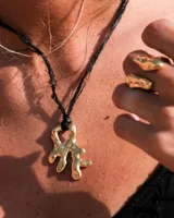 Collar con dije de bronce macizo con forma orgánica irregular, similar a un coral, suspendido de un cordón negro de seda natural anudado.