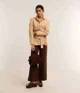 Pantalón wide leg de sarga color marrón, con cintura alta, trabillas, bolsillos delanteros y traseros, cierre con botón y cremallera, y costura vertical delantera.
