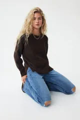 Jeans de denim azul medio con ligero efecto desgastado y roturas a la altura de las rodillas. Presenta un corte ajustado en muslos y acampanado desde la rodilla. El tiro es bajo, con pretina prolongada que se cierra con dos botones visibles. Incluye bolsillos delanteros tipo parche y bolsillos traseros.