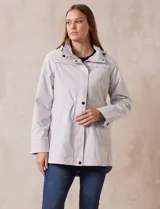 Campera impermeable color gris claro, marca Gallery. Tiene abertura central con cierre oculto y botones a presión, bolsillos delanteros y capucha plegable en el cuello.