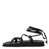 Sandalias planas negras con tiras finas y cordones para atar al tobillo.