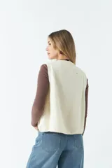 Chaleco de punto grueso color crema, con escote redondo y bordes acanalados.