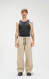 Pantalón deportivo beige de nylon con cintura elástica ajustable con cordón, corte amplio y aberturas laterales con broches.