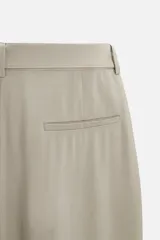 Pantalón negro de corte amplio, con pliegues frontales, bolsillos laterales y traseros de ojal. Incluye cinturón de la misma tela con hebilla metálica.