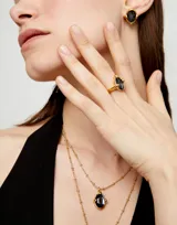 Anillo dorado con un cristal facetado gris en forma de lágrima.