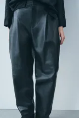 Pantalón de cuero negro de tiro medio, con pinzas delanteras, bolsillos laterales ocultos y corte holgado.