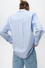 Camisa celeste y blanca a rayas verticales, de corte recto, con cuello solapa, escote pico y manga larga. Cierre frontal con botones.