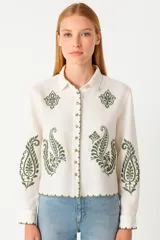 Camisa blanca de lino con bordados verdes de estilo paisley, cuello clásico, cierre frontal con botones y corte recto.