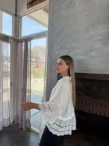 Camisa blanca de lino con cuello clásico, cierre frontal con botones, mangas 3/4 acampanadas con detalle de puntilla calada y ruedo con volados y puntilla calada.