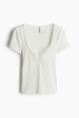 Remera corta blanca de punto suave con textura acanalada. Modelo ajustado con costura fruncida en el centro del busto y escote corazón pronunciado con ribete de picot.