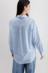 Camisa blanca a rayas verticales negras, de corte clásico, con cuello camisero y mangas largas con puños abotonados.