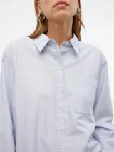 Camisa celeste de corte oversize, con cuello clásico, cierre frontal con botones, bolsillo en el pecho y mangas largas con puños abotonados.