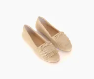 Mocasín color beige de cuero gamuzado con flecos y lazo con herrajes metálicos dorados en la capellada. Interior forrado en cuero y suela de goma flexible.