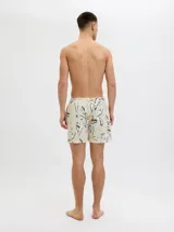 Short de baño color crema con estampado de flores y hojas en blanco, negro y amarillo. Tiene cintura elástica con cordón ajustable, bolsillos laterales y un bolsillo trasero.