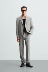 Pantalón de vestir gris claro, de corte recto, confeccionado en tejido con lana. Cuenta con bolsillos frontales y traseros de doble vivo con botón. Cierre frontal con cremallera y botón.