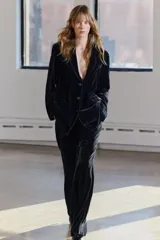 Pantalón de terciopelo negro de tiro medio, con bolsillos delanteros y traseros, pierna recta y cierre frontal con cremallera, botón y gancho metálico.