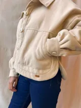 Chaqueta color beige con cuello camisero, cierre con botones a presión y bolsillos delanteros con solapa.
