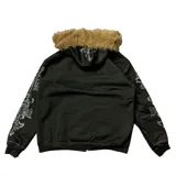 Campera negra con cierre frontal, capucha con borde de piel sintética removible, bolsillos laterales y apliques de strass plateados formando una cruz en el frente y diseños ornamentales en las mangas.