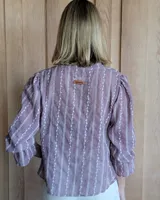 Blusa color beige con cuello con volados, mangas largas abullonadas con puños elásticos y cierre con botones en la parte delantera.