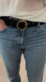 Cinturón negro de cuero con hebilla circular dorada.