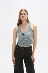 Chaleco de jean celeste sin mangas, con cuello en V, cierre frontal con botones y dos bolsillos con solapa en el pecho.
