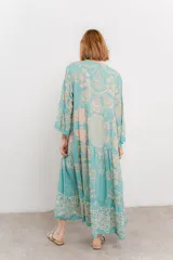 Vestido largo azul con estampado floral en tonos beige, confeccionado en viscosa. Presenta escote en V, botonadura completa en el frente y mangas largas con volados.