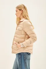 Campera puffer color beige con cuello camisero, cierre con botones a presión, bolsillos con solapa en el pecho y relleno de plumas.
