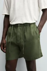 Bermuda negra regular fit confeccionada en tejido con mezcla de algodón y lino. Cintura elástica ajustable con cordón. Pliegues frontales. Bolsillos laterales y traseros de vivo. Cierre frontal con cremallera y botón.