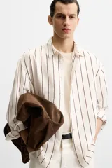 Camisa de hombre regular fit, color blanco con rayas verticales negras, cuello solapa, manga larga con puños abotonados y cierre frontal con botones.