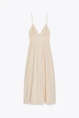Vestido midi color crema de popelín, con escote en pico, tirantes finos ajustables, bolsillos laterales ocultos y detalle de pliegues. Incluye forro interior.