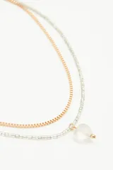 Collar doble, uno dorado y otro plateado, con dije de cristal transparente en forma de corazón.
