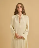 Vestido largo color crema, con cuello mao con lazo ajustable, mangas largas amplias y tajos laterales.